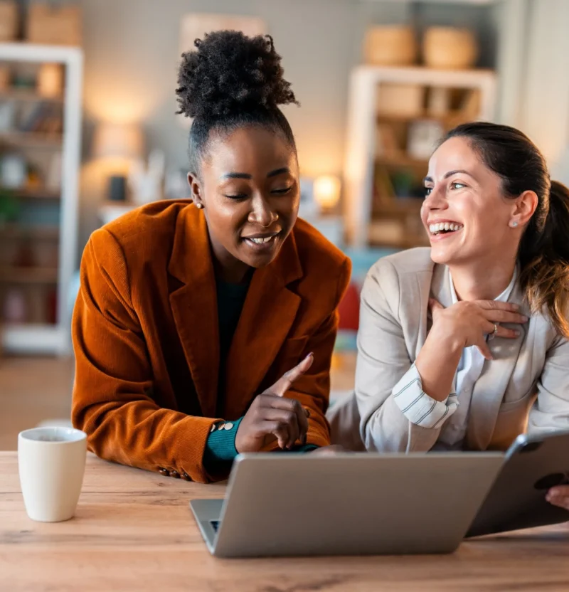 Two colleagues laughing over a laptop and tablet